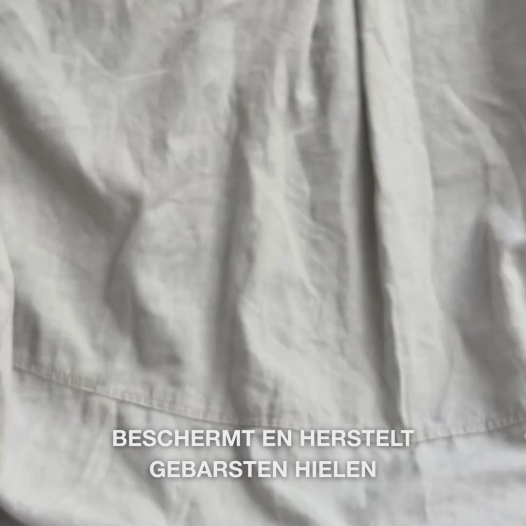 Close-up van een hand die een rijke, romige textuur van Heel Repair in de handpalm neemt en deze zachtjes op droge, gebarsten hielhuid masseert: de dikke substantie wordt zichtbaar opgenomen, verzacht en hydrateert ruwe huid, terwijl 25 % ureum, sheaboter en tea tree olie verzachtend en beschermend werken.