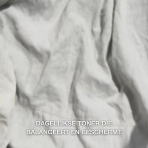 Close-up van een hand die enkele druppels van de heldere, waterige Face Tonic met Tea Tree Oil op een wattenschijfje druppelt en deze zacht over schone huid aanbrengt: de lichte, verfrissende vloeistof verzacht, reinigt diep, hydrateert en laat de huid vernieuwd achter, klaar voor een crème.