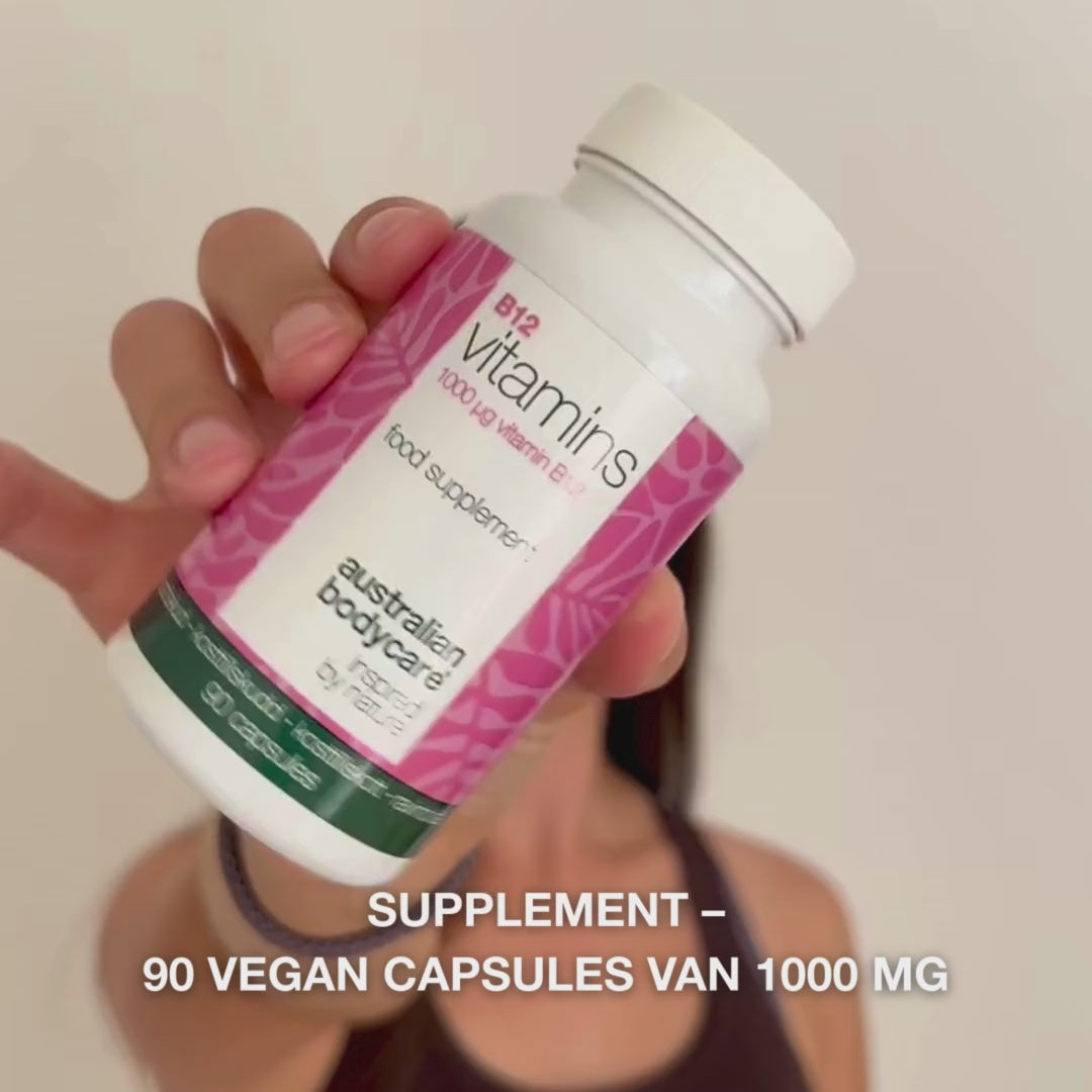 Close-up van een hand die het flesje met Vitamine B12 voedingssupplement vasthoudt, het deksel opent en gladde, witte capsules uitschenkt—het product voor dagelijks gebruik ter ondersteuning van energie, immuunsysteem, zenuwstelsel en vermindering van vermoeidheid.